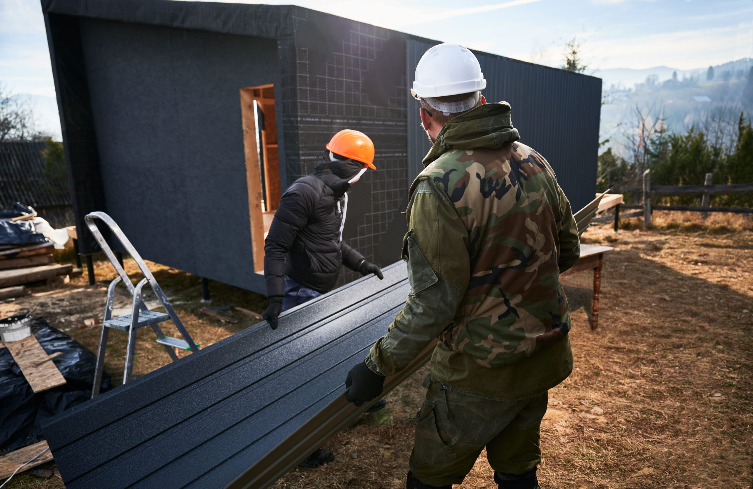 Builder installing corrugated iron sheet used as facade of future wooden frame house.