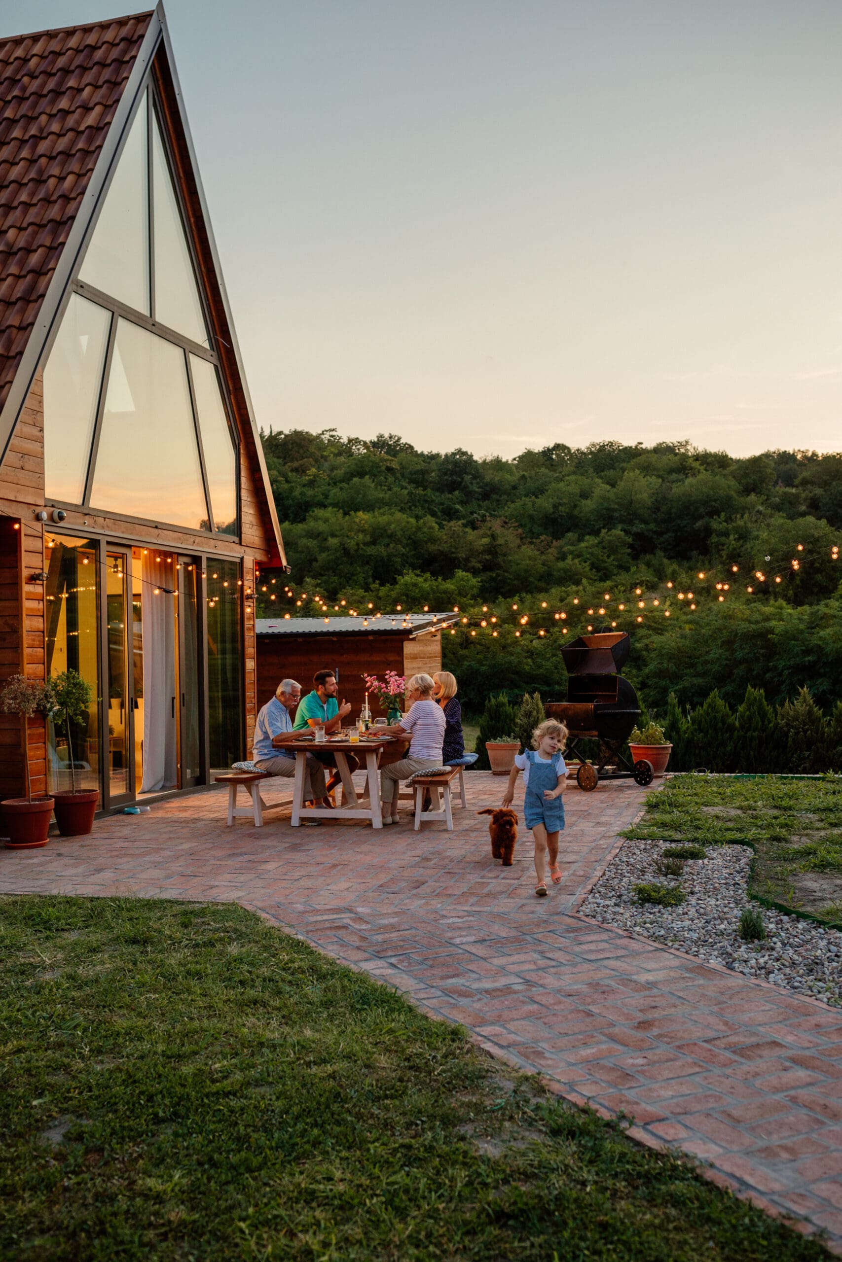 Girl and her dog is playing beside her family who having dinner in the backyard