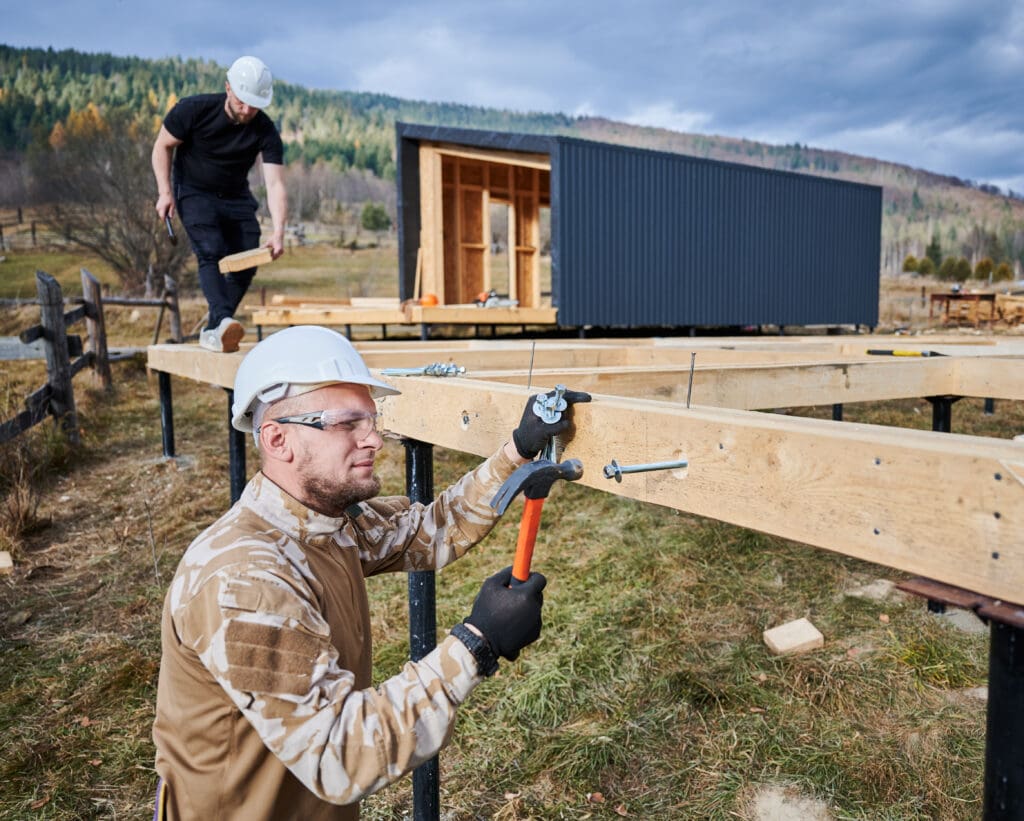 Man worker hammering while building wooden frame house.